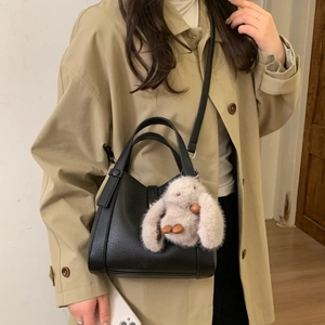 Litchi pattern leather bucket bag with plush rabbit charm shown on model in trench coat