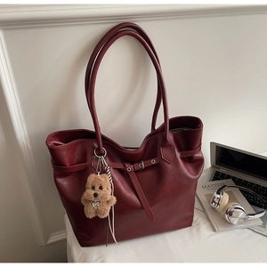 Detail view of burgundy tote bag with leather strap buckle and cute brown bear charm