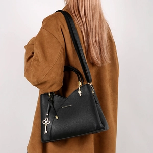 Detail view of black lychee leather bucket bag with gold charms on brown trench coat