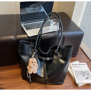 Close-up of black leather tote bag with plush puppy charm and decorative buckle detail