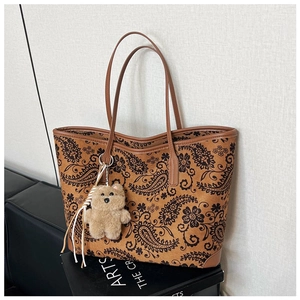 Detail of vintage paisley tote bag with smooth leather trim and plush bear charm