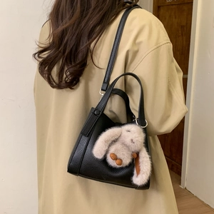 Detail shot of a black litchi grain bucket bag with a cute white rabbit plush charm