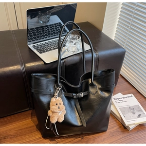 Black PU leather tote bag on leather stool with plush bear charm and notebook accessories