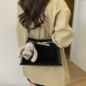 Detail of black retro bucket bag with gold clasp, leather texture and plush rabbit charm
