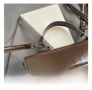Detail of metal hook and handle attachment on dark brown patent leather bag