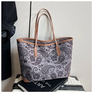 Detail of vintage paisley print tote bag with brown leather handles on white suitcase