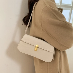 Detail of cream white leather baguette bag with gold clasp worn with beige wool coat