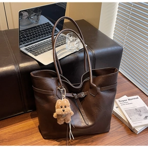 Detail of dark brown tote bag with bear charm on a bench with laptop and books