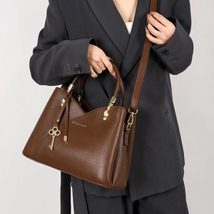 Detail of dark brown pebble leather handbag with gold key charm and musical note hardware