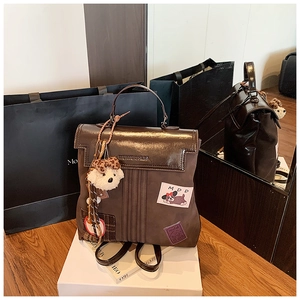 Détail d'un sac à dos marron foncé avec rabat verni et breloque ours en peluche
