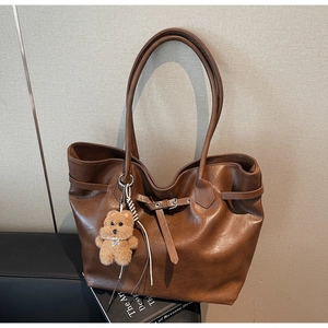 Detail view of large dark brown leather tote bag with plush bear charm on a stack of books