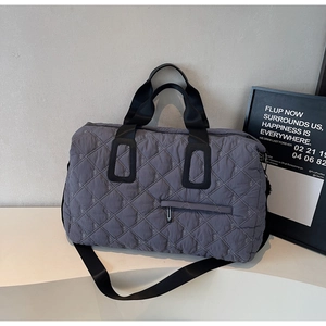 Detail of grey quilted travel bag with diamond patterns and black woven handles