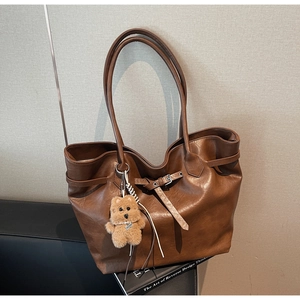 Detailed close-up of brown faux leather tote bag with metal buckle and plush bear charm