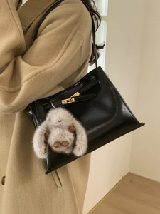 Retro black leather bucket bag with gold clasp and plush charm on khaki coat