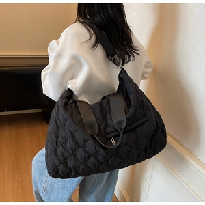 Detail of black quilted tote bag with diamond pattern shown on model in indoor setting
