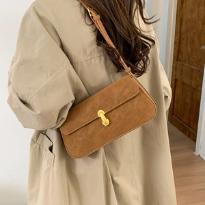 Brown suede shoulder bag with gold oval metal buckle worn by model in beige trench coat