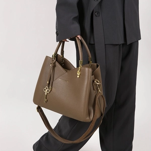 Detail of dark brown leather bucket bag with gold charms and adjustable shoulder strap