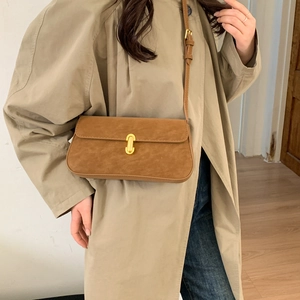 Detail shot of a dark brown suede crossbody bag with gold buckle on a beige trench coat