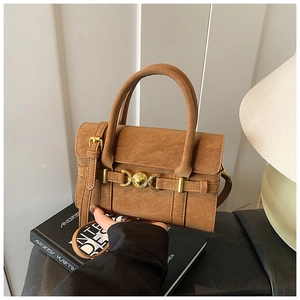 Detail view of tan crossbody bag with golden hardware resting on designer books