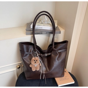 Detail of a large chocolate faux leather tote bag with a belt buckle and plush bear charm