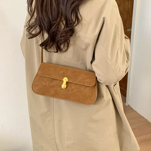Close-up of brown suede underarm bag with gold U-shaped rotating lock on beige coat