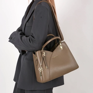 Detail of taupe lychee leather texture and G-clef metal hardware on a shoulder bag