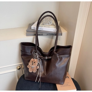 Detail of dark coffee faux leather tote bag featuring metal buckle and cute bear charm