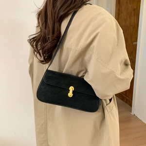Detail of a black suede underarm bag with a gold U-shaped buckle on a beige coat