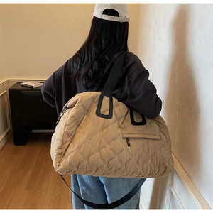 Close-up of beige quilted tote bag with side zipper pocket and black strap