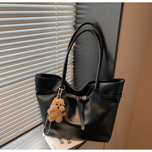 Detail of black leather tote bag featuring a decorative buckle and plush bear pendant