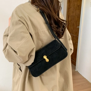 Detail of a black suede underarm bag with a sleek gold buckle on a khaki trench coat