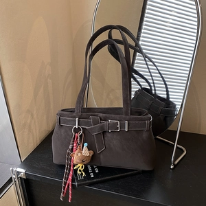 Detail of dark brown matte tote bag featuring a decorative buckle and plush bear charm