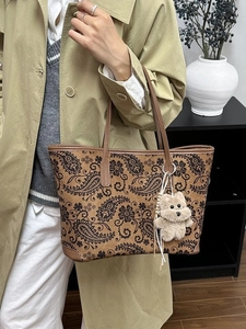 Brown paisley print tote bag with plush bear charm shown in a modern interior setting
