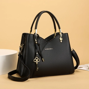 Detail of black pebbled leather handbag with gold key charm and music note hardware