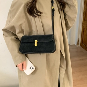 Detailed view of black suede baguette bag featuring an elegant gold oval metal lock
