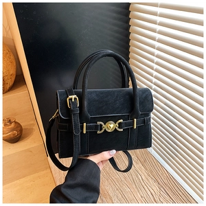 Close-up of black crossbody bag with vintage gold heart buckle and leather texture