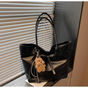 Close-up of black tote bag with decorative straps and a cute plush bear charm detail