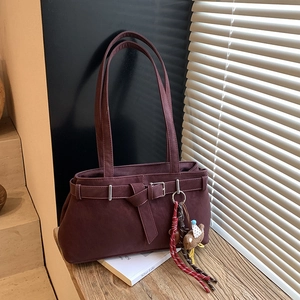 Detail of burgundy tote bag with buckle strap and cute teddy bear keychain charm
