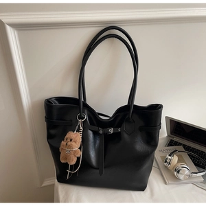 Macro view of black leather tote bag with elegant buckle detail and plush bear charm