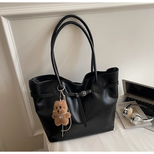 Detail of black glossy PU tote bag with bear charm and adjustable strap on a minimalist desk