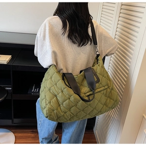 Detailed view of olive green quilted puffer tote bag with black canvas straps on model