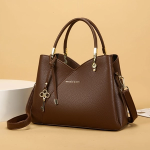 Detail view of brown lychee grain leather handbag with gold key and clef charms