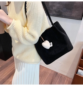 Detail of black suede tote bag with heart charm and stay dry tag on white skirt