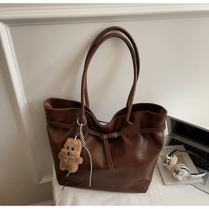 Close-up of large brown leather tote bag with decorative buckle and plush bear pendant