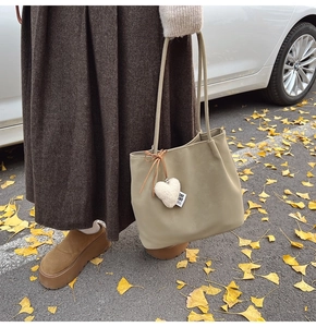 Detail of suede tote bag with heart charm on a background of golden ginkgo leaves