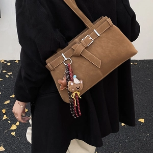 Close-up of caramel suede shoulder bag with belt buckle and cute bear charm detail