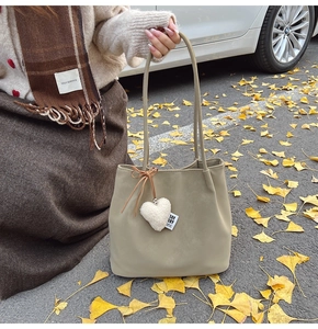 Detail of suede tote bag in beige with a plush heart charm against an autumn backdrop