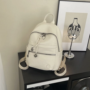 Detailed macro view of beige lychee grain leather backpack with silver zippers and charm