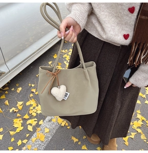 Close-up of khaki suede bucket bag featuring plush heart charm and autumn leaf background