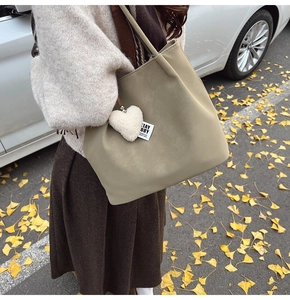 Detail of sage green vintage tote bag with heart charm shown on model in outdoor autumn setting